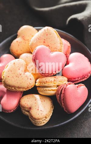 Heart shaped Sweet macarons on plate on black table. Stock Photo