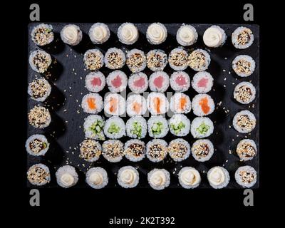 Top view of an assortment of different types of sushi rolls placed on a black stone board. Stock Photo