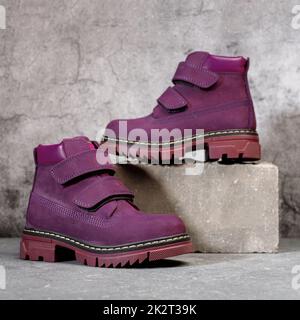 Stylish waterproof burgundy women's boots with velcro on a gray concrete background. Stock Photo