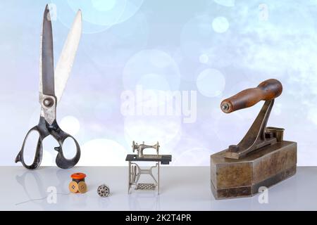 Professional old large tailor scissors, large tailor iron miniature model of a sewing machine and accessories on table with blue background. Advertisment for tailor business. Space for text and montage. Stock Photo