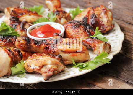 Grilled chicken legs on wooden table served on white plate with coriander Stock Photo