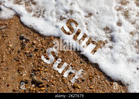 Surf text cut out on both pebble beach and lapping waves Stock Photo