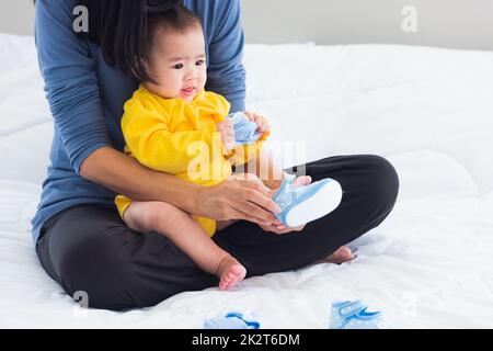 mother sitting on the bed wearing shoes to his cute baby little girl toddler on bedroom Stock Photo