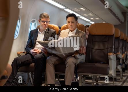 Businessman in brown suit on trip holding business newspaper while reading in plane during flight . Stock Photo