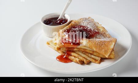 French crepes for Breakfast with strawberry jam.  Wheat golden yeast pancakes or crepes in a white plate closeup. Stock Photo
