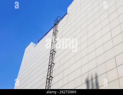 Outdoor fire escape on the wall of an office or industrial building. Bottom-up view. Fire escape on the facade of the building for access to the roof in emergency situations Stock Photo