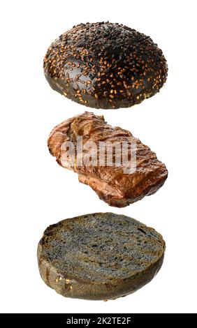 A fried piece of pork meat and two halves of a rye flour bun with sesame seeds levitate on a white background Stock Photo