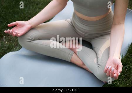 A young woman meditates sitting in a park on the green grass on a warm summer day. Stock Photo