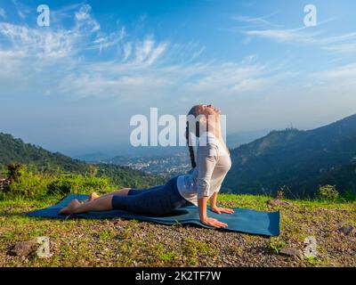 Woman practices yoga asana Urdhva Mukha Svanasana outdoors Stock Photo