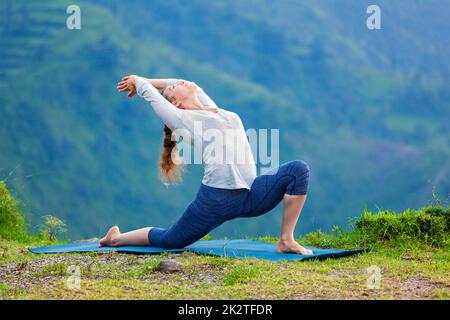 Sporty fit woman practices yoga asana Anjaneyasana in mountains Stock Photo