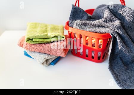 Multi-colored towels lie in a red laundry basket on a white background. Washing and ironing clothes, top view. Stock Photo