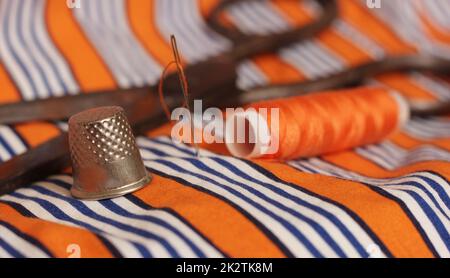 Orange Thread and Thimble on Orange and White Striped Fabric Stock Photo