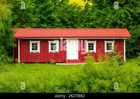 Red wooden house in a nature with a lot of green trees and lawn Stock Photo