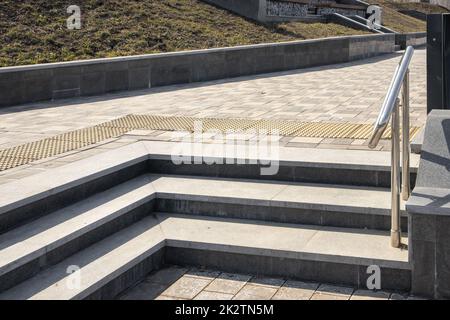 Close-up of granite stone steps located at an angle, in a metal railing, outdoors, in a city park Stock Photo