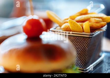 Focus in the background on french fries in a mesh basket standing near a burger Stock Photo