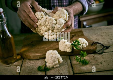 Anonymous male dividing cauliflower on rustic table Stock Photo
