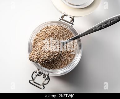 Glass container with spoon and white chia seeds placed on white ...