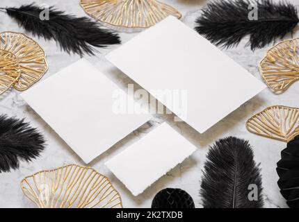 Blank cards on marble table near black feathers and golden leaves close up. Wedding set mockup Stock Photo