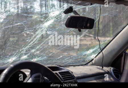Broken windshield of a car from a bullet, from a shot from a firearm, view from the inside of the cabin. Damaged glass with traces of an oncoming stone on the road. Interior view of the car. Stock Photo