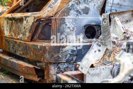 The car was completely destroyed by fire. Abandoned, burnt and rusty car by the road. Cars were on fire in the parking lot. War of Russia against Ukraine. Shrapnel and bullet holes in cars. Stock Photo