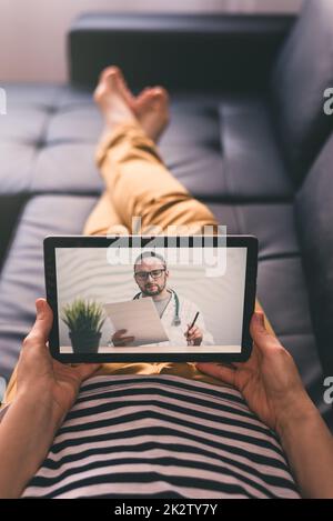 Woman lying on a sofa and talking with a doctor online using digital tablet. Telemedicine concept. Stock Photo