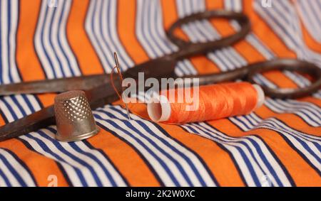 Orange Thread and Thimble on Orange and White Striped Fabric Stock Photo