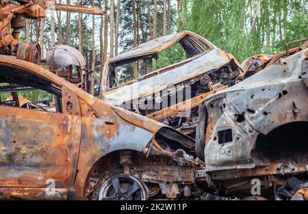 A view of burnt-out cars after rocket attacks by the Russian military. War of Russia against Ukraine. Civil vehicle after the fire. Cemetery of cars in the city of Irpin. Rusty pile of metal. Stock Photo