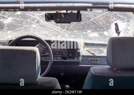Broken windshield of a car from a bullet, from a shot from a firearm, view from the inside of the cabin. Damaged glass with traces of an oncoming stone on the road. Interior view of the car. Stock Photo