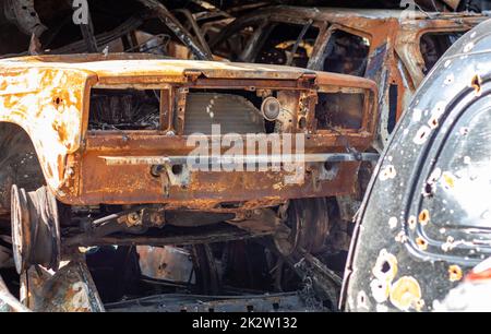 The car burned down completely, even the tires burned out. Burnt out car crash after fire. The bomb shell of the terrorist attack blew up civilians. Disaster zone. Abandoned car on the road. Stock Photo