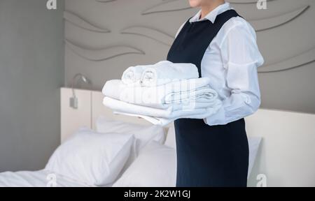 Room service maid holding clean folded white towels in hotel guest room. Stock Photo