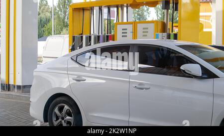 The white car is refueling. Refueling a car parked at a gas station. Refuel cars with petrol pump at gas stations. Energy of oil and gas. Fuel shortage in Ukraine. Image of pumps at a gas station. Stock Photo
