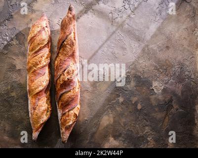 Two freshly baked baguettes on a stone background. Stock Photo