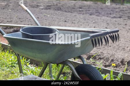 Gray metal garden wheelbarrow with two handles and one wheel. The wheelbarrow is in the garden or garden. Gardener's wheelbarrow in the backyard. Garden cleaning. Stock Photo