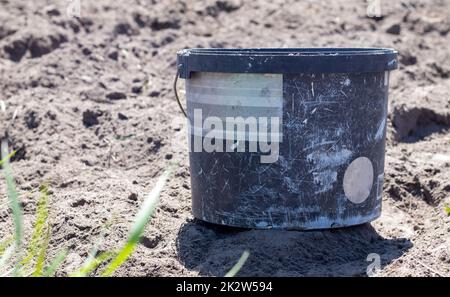 Plastic dirty garden bucket, container with handle on vegetable garden on loose ground. Garden equipment. Bright sunny day in the garden. Stock Photo