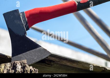 A new modern ax with a red handle sticks out of a wooden stump against a green meadow on a summer sunny day. The ax stuck into the stump. Ax blade in a log. Stock Photo