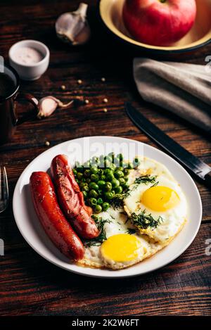 Breakfast with fried eggs, sausages and green peas Stock Photo