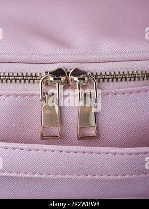 gold zippers with gold zippers are fastened on a pink leather object, close-up Stock Photo