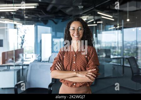 Young successful Indian IT developer female engineer working inside the office of a development company portrait of a female programmer with curly hair and glasses, smiling and looking at the camera. Stock Photo
