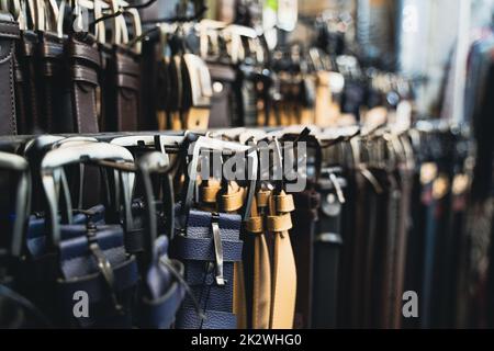 perspective view closeup of different kinds of leather colored belts for jeans and suits trousers hanging by the buckle in clothes store display Stock Photo