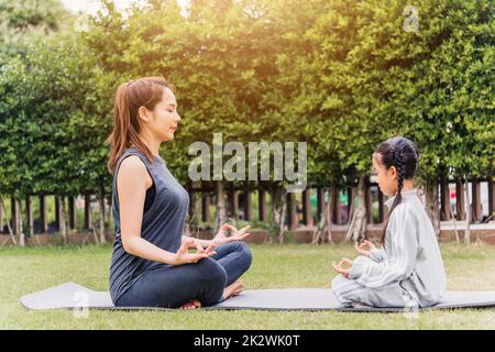 mother practicing doing yoga exercises with her daughter outdoors in meditate pose together Stock Photo