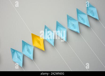 A row of paper boats on a gray background, yellow is moving in the opposite direction Stock Photo