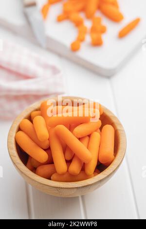 Baby carrot vegetable in bowl. Mini orange carrots on white table. Stock Photo