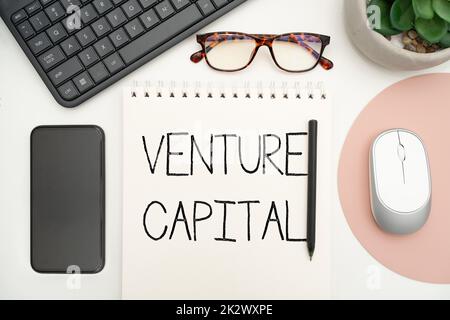 Text sign showing Venture Capital. Internet Concept financing provided by firms to small early stage ones Office Supplies Over Desk With Keyboard And Glasses And Coffee Cup For Working Stock Photo