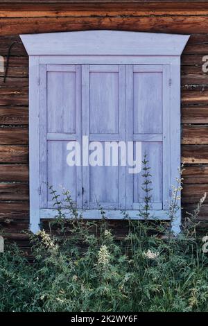 Old wooden window with closed shabby shutters lavender color. Facade of typical rural timber house, Russia Stock Photo