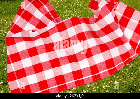 Picnic background. Red checkered picnic cloth on blurred sun-flooded lush grass with focus on napkkin. Beautiful backdrop for your product placement or montage. Stock Photo