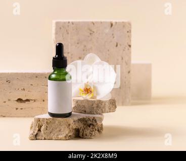 Green dropper glass bottle near white orchid flower on light yellow, Mockup. Skincare product Stock Photo