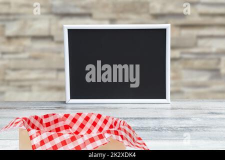 Food recipe template. Empty black board and picnic basket on a rustic wooden table over blurred stone wall background. For your food product placement or montage. Copy space. Stock Photo