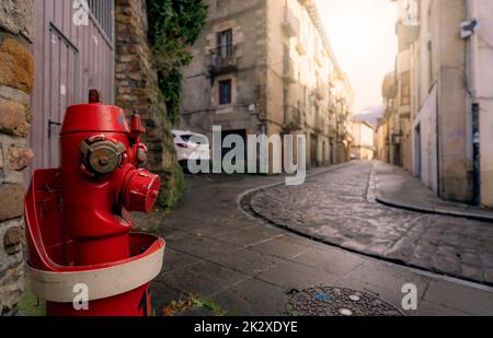 Red fire hydrant on sidewalk in Onati city, Spain. Fire hydrant on blur old building, white car, and street. Cityscape. Water supply for fire extinguisher. Fire control system of the city for safety. Stock Photo