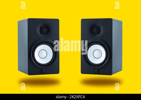 Pair of professional high quality monitor speakers for sound recording, mixing, and mastering in studio in black wooden casing isolated on yellow background. Front or Side view. Stock Photo