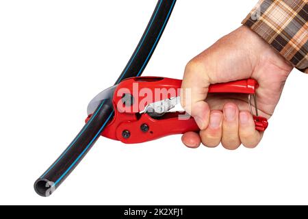 Plumber tools isolated. A man accurately cuts a piece of PE pressure pipe or water pipe with a red pvc pipe cutter. Clipping path. Drinking and service water systems. Stock Photo